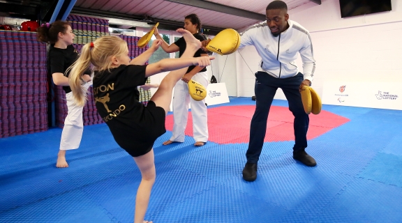 Young child kicking into the pads held by Olympian Lutalo Muhammad at a Taekwondo club in Liverpool