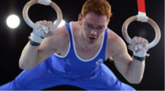 Male gymnast dressed in blue, competing on the rings.