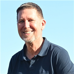 Man with short brown hair and beard, smiling. Wearing a blue polo shirt.