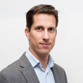 Headshot photo of Simon Morton. A white man with short brown hair wearing a light blue shirt and grey blazer.