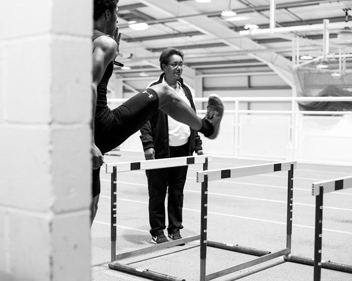 a coach watching over an athlete doing hurdles
