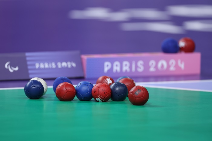 Blue and red boccia balls lie on the field of play with the Paris 2024 logo in the background.