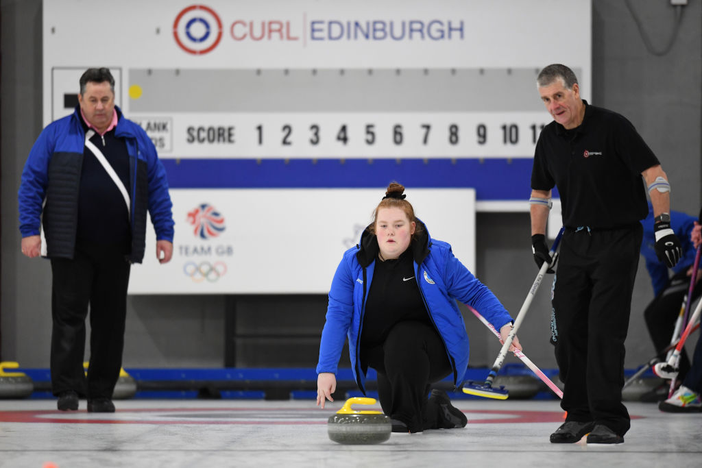 young curler on the ice with his coach standing above him