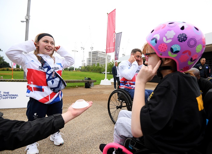 Ellie is standing opposite a young child in a wheelchair playing a game at the Olympic Park in London