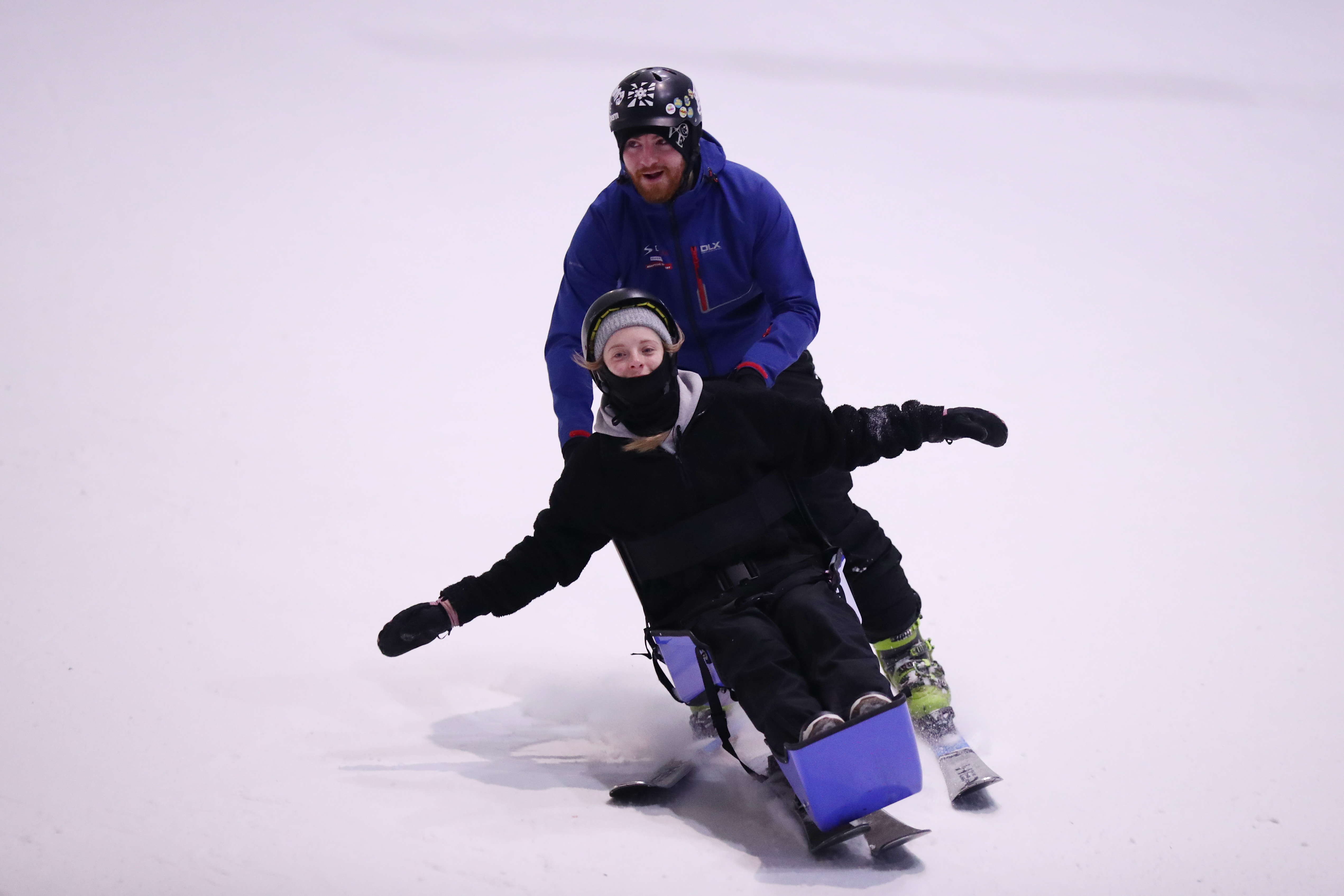 Two people skiing, one in a skisled and guided by another skier