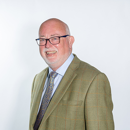 A man in a shirt and tie and green jacket - wearing glasses he has a smile with a white beard.
