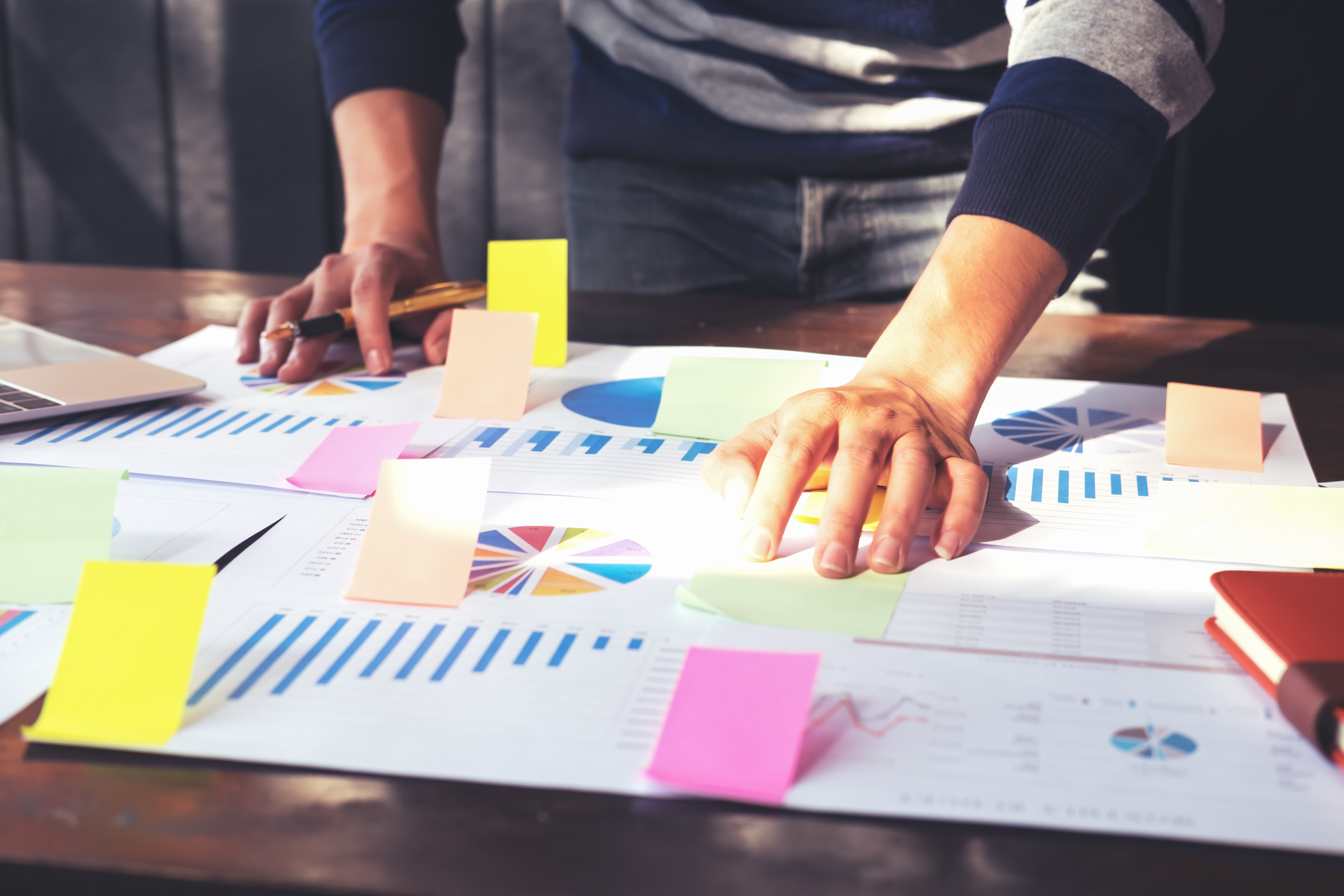 Photography of a persons hands leaning over planning documents and post it notes