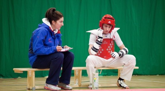 A Taekwondo athlete and coach sat on a bench seat during a training session