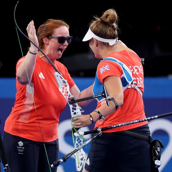 Two people embrace each other smiling during a sporting competition. One holds an bow whilst embracing - celebrating a good shot.