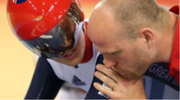 Track cyclist sat on a bike being given instruction by their coach