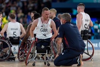 Two people talk. Once is in a wheelchair having played Wheelchair Rugby with GBR written on his jersey.