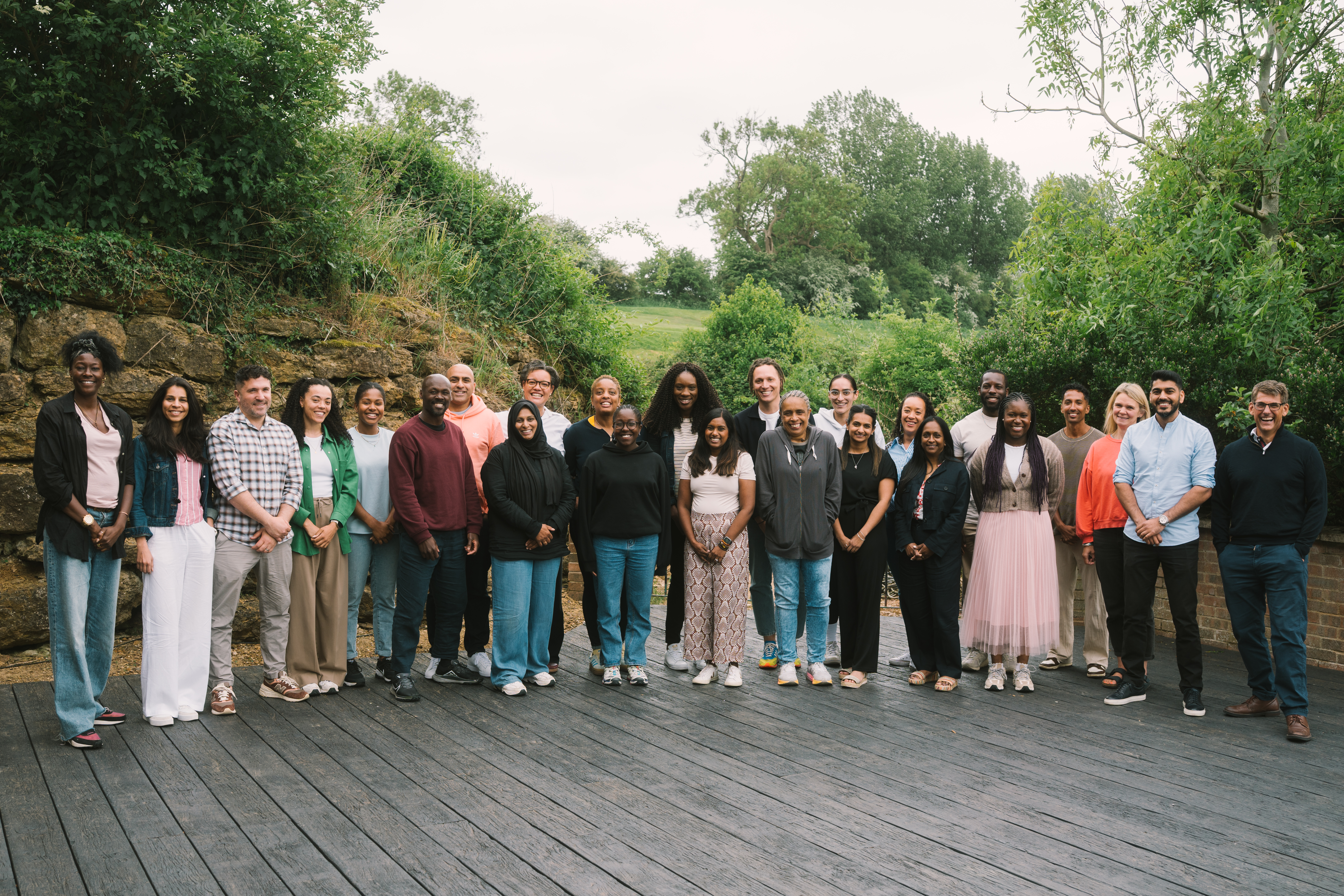 A group of people of different genders, backgrounds and ages stood on a wooden deck overlooking trees