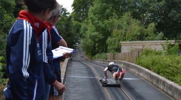 Two coaches, one holding a clipboard. Watching a skeleton athlete training on a push track.