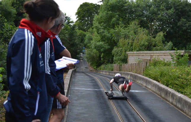 Two coaches, one holding a clipboard. Watching a skeleton athlete training on a push track.