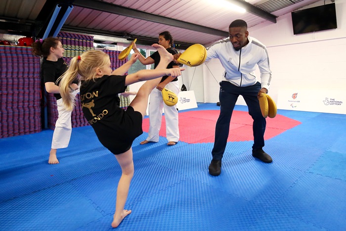 A black male athlete working on a kicking training exercise with a female child at a Taekwondo