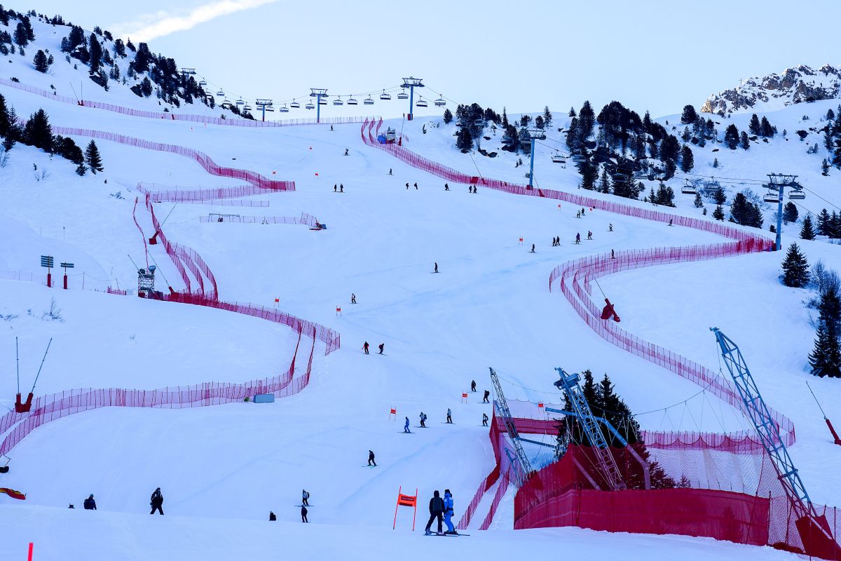 Copilot said:  Snow-covered ski slope with skiers, chairlifts and red safety fencing on a mountain.