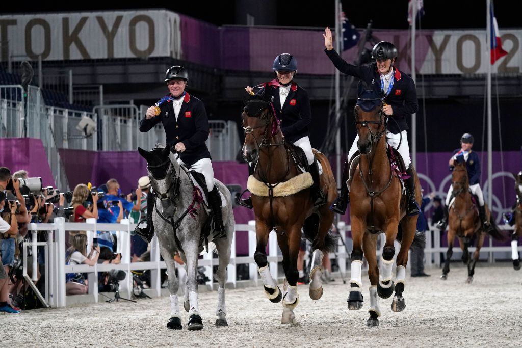 Britain's team Tom McEwen, Laura Collett and Oliver Townend display their gold medals as they ride in the ring after winning the the equestrian eventing jumping teams final during the Tokyo 2020 Olympic Games at the Equestrian Park in Tokyo