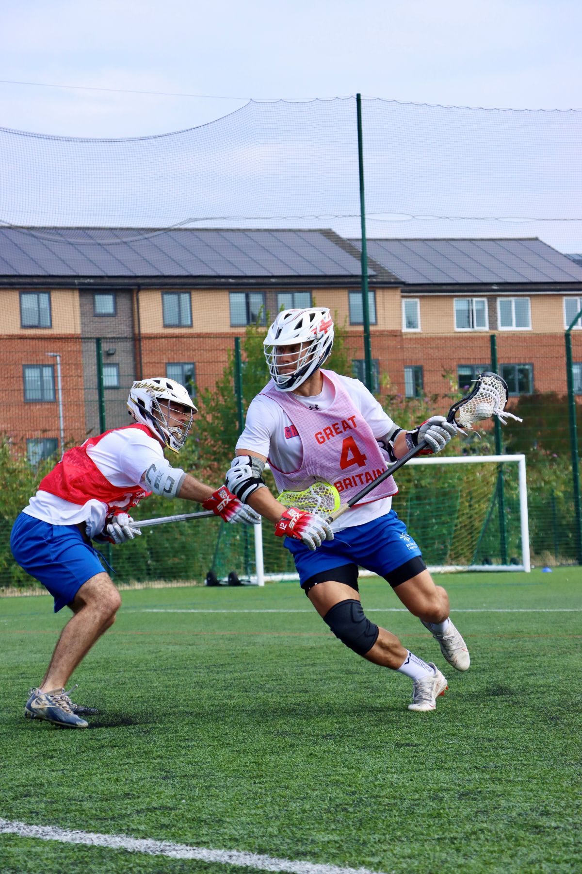 A man holding a lacrosse stick in GB kit mid games.