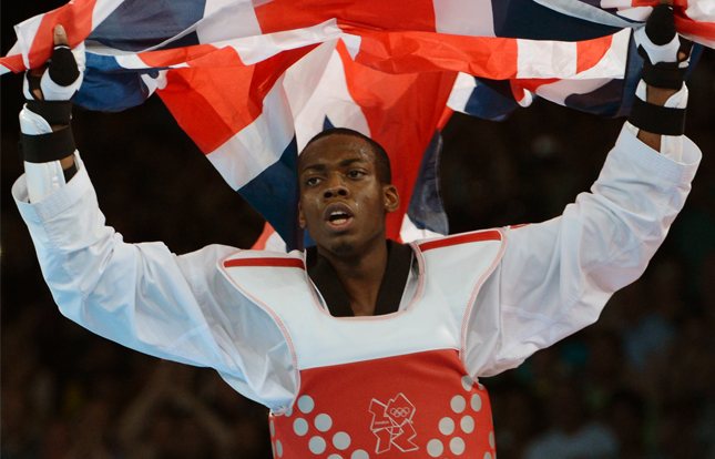Lutalo Muhammad dressed in taekwondo kit, holding a union jack flag above his head in celebration