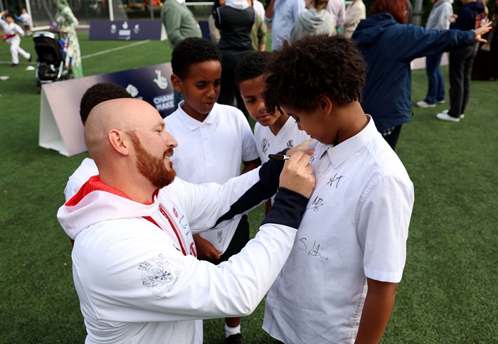 Paralympic Champion Dan Pembroke attends a ChangeMaker Event. A group of children stand around him and he is placing his signature on the t-shirt of one of the children.