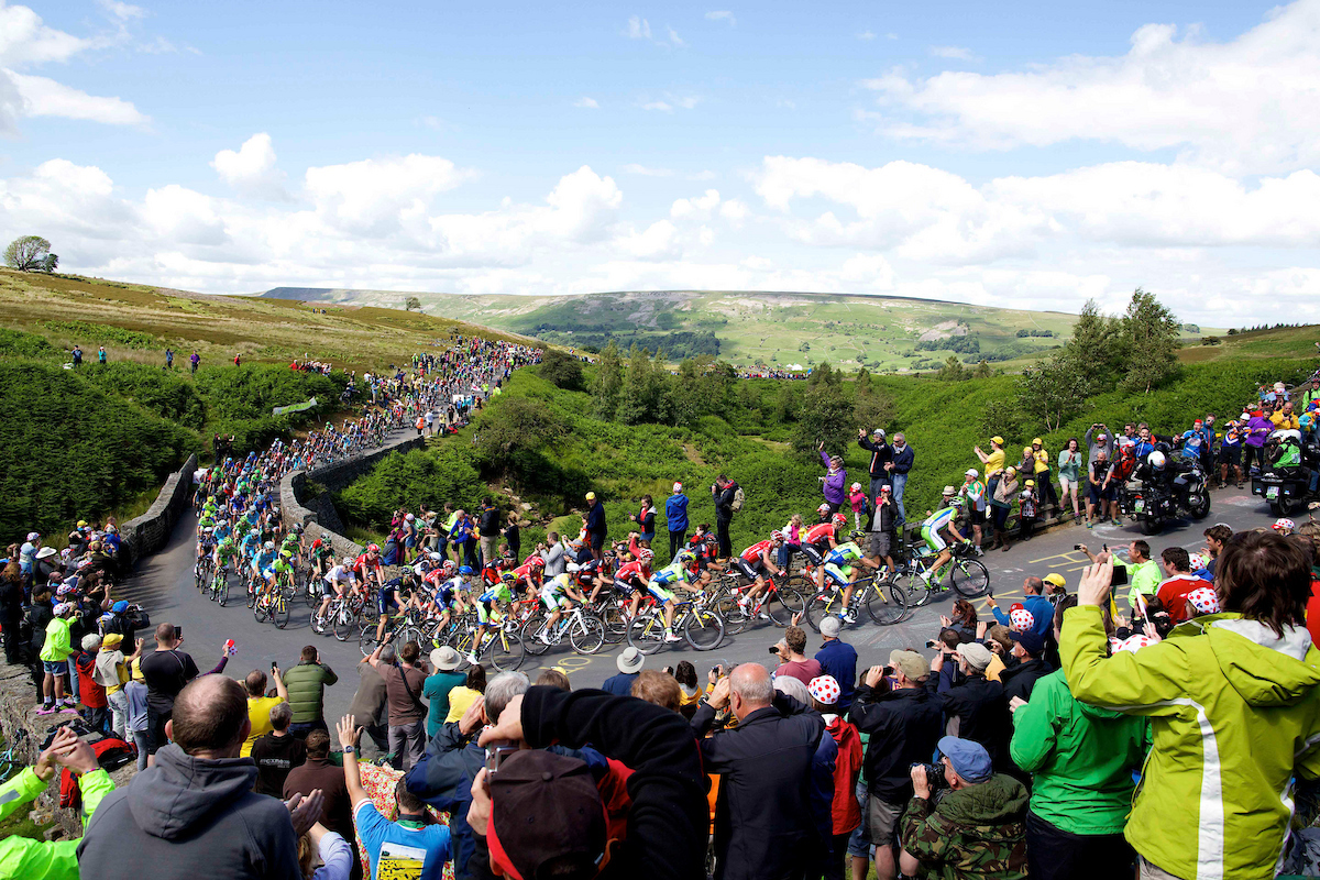 Crowds line the road and take pictures as the peloton of bike riders ride past during the Tour de France 2014 Grand Depart - Stage 1, Leeds to Harrogate - Yorkshire, England - Grinton Moor, Yokshire Dales. 