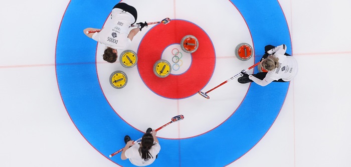 Ariel photograph of three Team GB curling athletes stood over the house on a curling ice sheet at the Beijing 2022 Winter Olympics