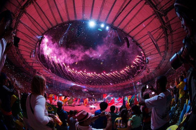A crowded sports stadium, lit by fireworks at the opening ceremony of the Olympic games 