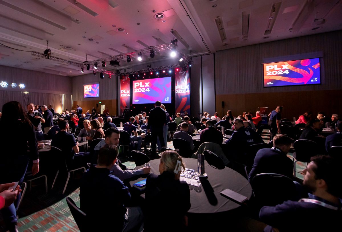 A view of a stage with people sat in a room waiting for a speak, the lighting is blue and red.